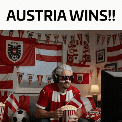 A Man Sitting On A Couch Holding A Popcorn Bucket That Says Austria Wins GIF