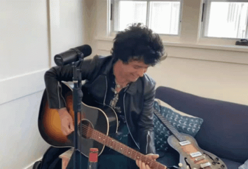 A Man Sitting On A Couch Playing A Guitar GIF
