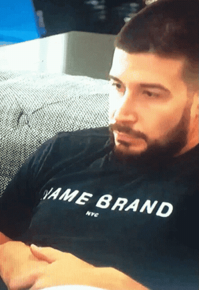 A Man Sitting On A Couch Wearing A Black Shirt That Says Name Brand Nyc GIF