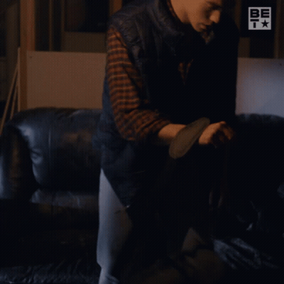 A Man Sitting On A Couch With A Be T Logo On The Wall Behind Him GIF