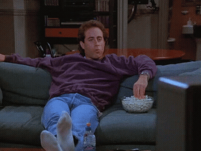 A Man Sitting On A Couch With A Bowl Of Popcorn In Front Of Him GIF