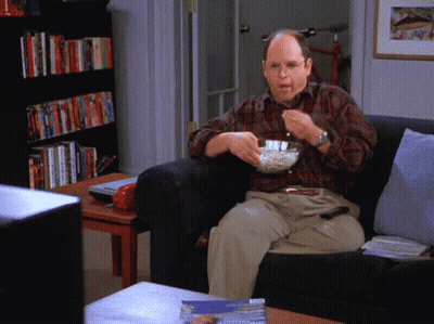 A Man Sitting On A Couch With A Bowl Of Popcorn In His Hand GIF