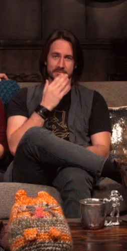 A Man Sitting On A Couch With A Knitted Cat Hat GIF