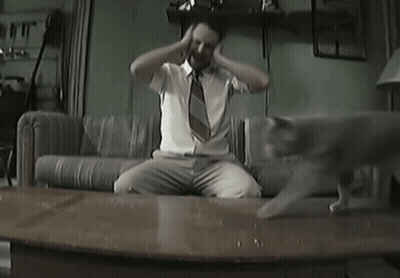 A Man Sitting On A Couch With His Hands On His Head GIF