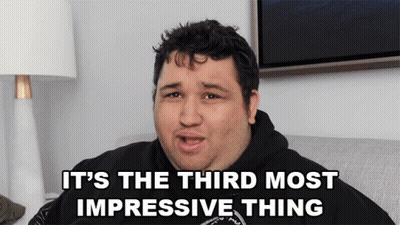 A Man Sitting On A Couch With The Words It 'S The Third Most Impressive Thing Above Him GIF