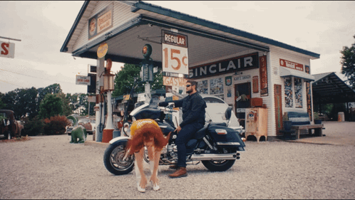A Man Sitting On A Motorcycle In Front Of A Gas Station That Says Regular 15 Cents GIF