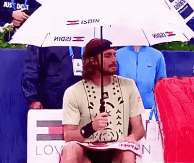A Man Sitting Under An Umbrella That Says Isdin On It GIF