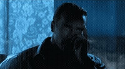 A Man Smoking A Cigarette In A Dark Room With A Blue Background GIF