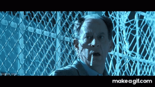 A Man Smoking A Cigarette In Front Of A Chain Link Fence With Make A Gif.com In The Corner GIF