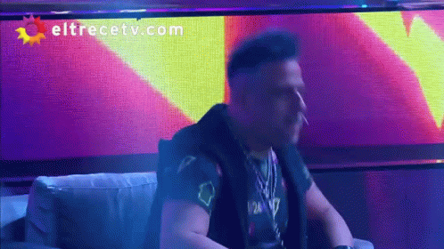 A Man Smoking A Cigarette In Front Of A Eltrecetv.com Sign GIF