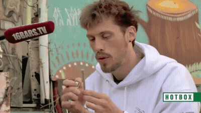 A Man Smoking A Cigarette In Front Of A Hotbox Sign GIF
