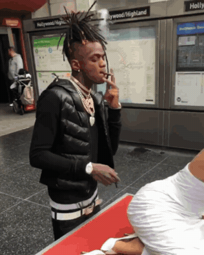 A Man Smoking A Cigarette In Front Of A Sign That Says Hollywood / Highland GIF