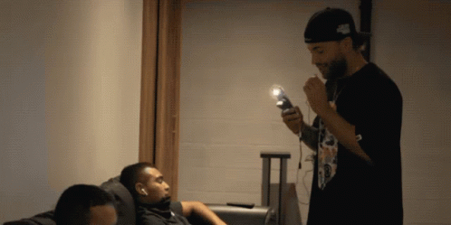 A Man Smoking A Cigarette While Another Man Sits On The Couch GIF