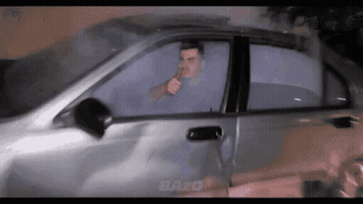 A Man Smoking A Cigarette While Driving A Car With The Word Bazo On The Bottom GIF