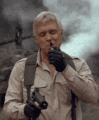 A Man Smoking A Cigarette While Holding A Gun In His Hand GIF
