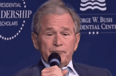 A Man Speaking Into A Microphone In Front Of A Sign That Says George W. Bush Presidential Center GIF