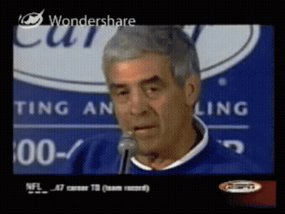 A Man Speaking Into A Microphone In Front Of A Sign That Says Ting An Ling GIF