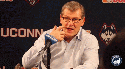 A Man Speaking Into A Microphone In Front Of A Uconn Logo GIF