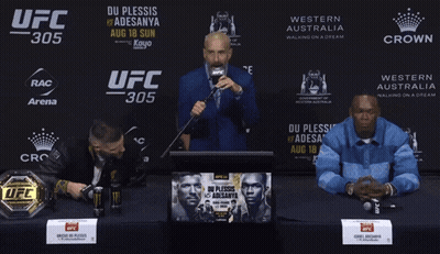 A Man Speaking Into A Microphone In Front Of A Ufc 305 Banner GIF