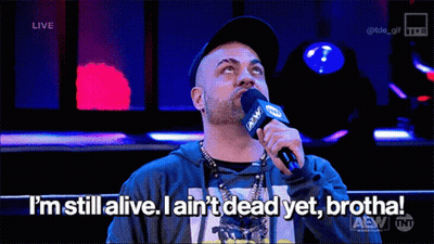 A Man Speaking Into A Microphone That Says I 'M Still Alive GIF