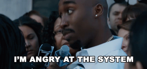 A Man Speaking Into A Microphone With The Words " I 'M Angry At The System " Above Him GIF