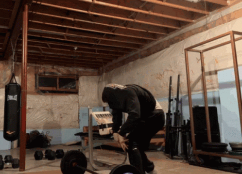 A Man Squatting In A Gym With A Everlast Punching Bag In The Background GIF