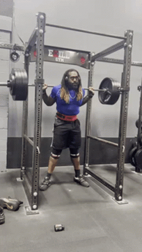 A Man Squatting With A Barbell In Front Of An Evil Gym Sign GIF