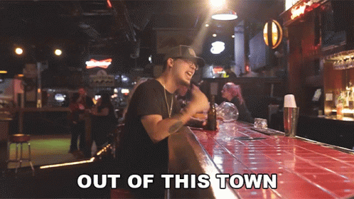 A Man Standing At A Bar With Out Of This Town Written On The Bottom GIF