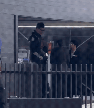A Man Standing Behind A Fence Talking To A Man In A Suit GIF