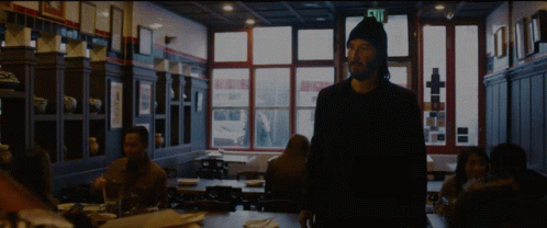A Man Standing In A Dark Room With A Sign That Says Exit GIF