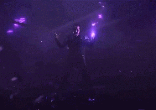 A Man Standing In A Dark Room With Purple Lights Around Him GIF