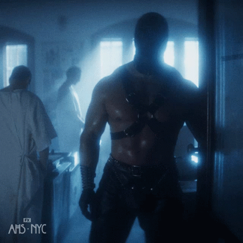 A Man Standing In A Dark Room With The Letters Ahs Nyc On The Bottom Left GIF
