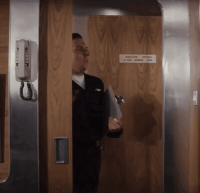 A Man Standing In A Doorway With A Sign That Says Executive Officer GIF