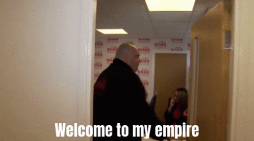 A Man Standing In A Hallway With The Words Welcome To My Empire Written On The Wall Behind Him GIF