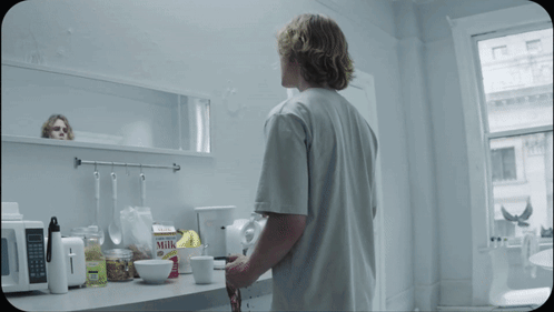 A Man Standing In A Kitchen Looking At A Box Of Milk GIF
