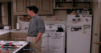 A Man Standing In A Kitchen Next To A White Refrigerator GIF