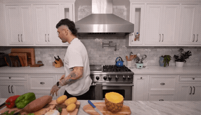 A Man Standing In A Kitchen With A Pineapple Sliced In Half On A Cutting Board GIF