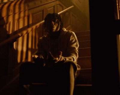 A Man Standing In A Room With White Curtains And A Necklace With The Letter O On It GIF