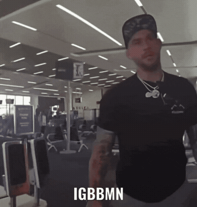 A Man Standing In An Airport With Igbbmn Written On The Bottom Of His Shirt GIF