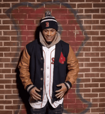 A Man Standing In Front Of A Brick Wall Wearing A Hat With The Letter B On It GIF