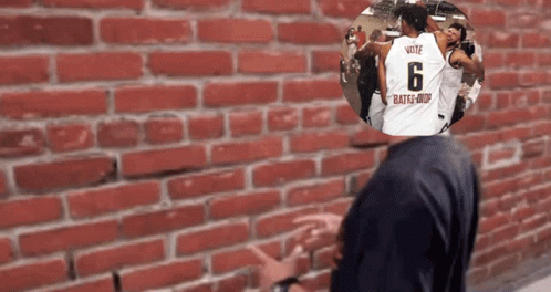 A Man Standing In Front Of A Brick Wall With A Picture Of A Man Wearing A Jersey With The Number 6 On It GIF