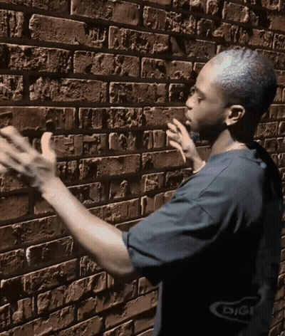 A Man Standing In Front Of A Brick Wall With The Word Digi On The Bottom Right GIF