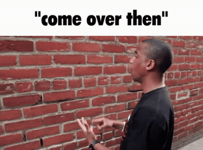 A Man Standing In Front Of A Brick Wall With The Words " Come Over Then " Written Above Him GIF
