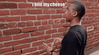 A Man Standing In Front Of A Brick Wall With The Words " I Bite My Cheese " Above Him GIF