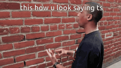A Man Standing In Front Of A Brick Wall With The Words This How U Look Saying Ts GIF