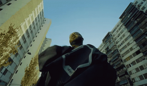 A Man Standing In Front Of A Building With The Word Trust On His Shirt GIF