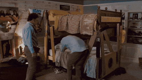 A Man Standing In Front Of A Bunk Bed With A Poster On The Wall That Says ' Boom ! ' GIF