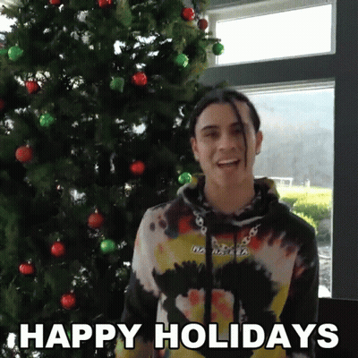 A Man Standing In Front Of A Christmas Tree With The Words Happy Holidays On The Bottom GIF
