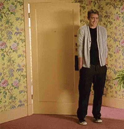A Man Standing In Front Of A Door With Floral Wallpaper On The Wall GIF
