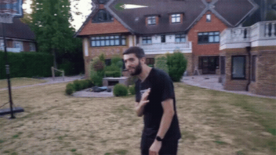 A Man Standing In Front Of A Large House With A Basketball Hoop In The Backyard GIF